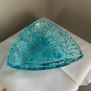 May include: A triangular glass serving dish with a light blue color and a floral pattern. The dish has three feet.