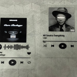 May include: Two black and white Spotify music player stickers. The left sticker features a black and white photo of a car with the text "Drake Care Package" and a Spotify barcode. The right sticker features a black and white photo of a man wearing a hat and the text "All Sinatra Everything Logic".