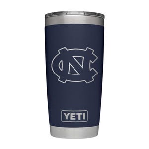 May include: Navy blue insulated tumbler with a silver lid and base. The tumbler features a white outline of the UNC logo and the brand name "YETI" in a white rectangular box.
