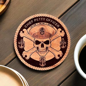 May include: A round wooden coaster with a dark brown background and a rope border. The center features a skull and crossbones with a navy hat on top. The text "CHIEF PETTY OFFICER" is written around the top of the coaster. The text "NAVY CHIEF EST. 1883 NAVY PRIDE" is written around the bottom of the coaster. The text "USN" is written three times on the coaster.