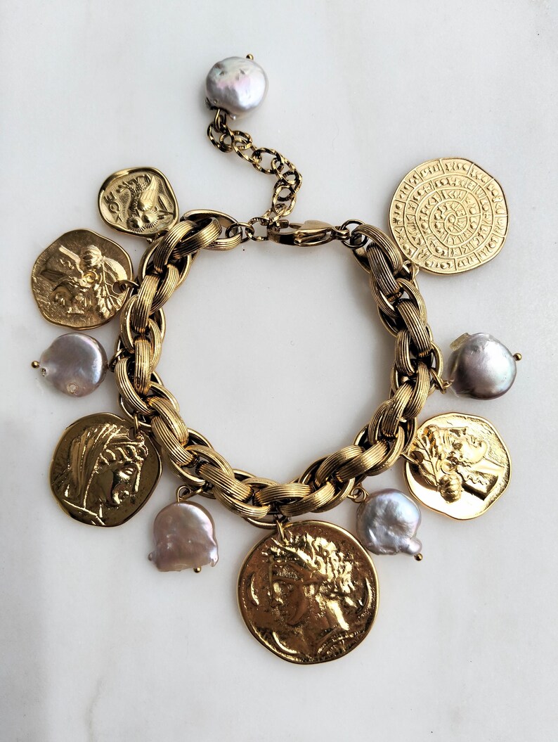 May include: A gold-toned bracelet featuring a chunky chain design, adorned with coin charms and irregular-shaped pearls. The coins display detailed relief patterns. The bracelet is displayed on a white surface.