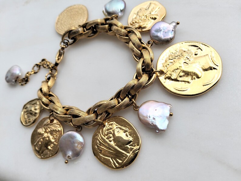 May include: Gold-toned charm bracelet featuring a braided chain design. The bracelet is adorned with coin-shaped charms and irregularly shaped pearls. The charms depict classical figures. The bracelet is a statement piece.