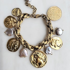 May include: Gold-toned bracelet featuring a chunky chain design, adorned with coin charms and irregular-shaped pearls. The coins display detailed relief patterns. The bracelet is set against a white background, highlighting its metallic sheen and intricate details.