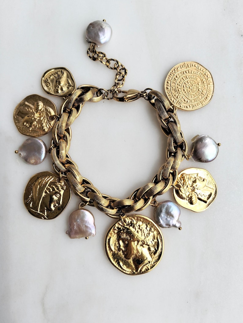 May include: Gold-toned bracelet featuring a chunky chain design, adorned with coin charms and irregular-shaped pearls. The coins display detailed relief patterns. The bracelet is set against a white background, highlighting its metallic sheen and intricate details.