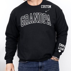 Peut inclure: Sweat-shirt noir avec un texte blanc qui dit "GRANDPA" dans une police d'écriture universitaire. Le texte "CUSTOM" est écrit au-dessus du mot "GRANDPA" avec une flèche qui pointe vers lui. Le texte "EMMA LIAM" est écrit sur la manche gauche avec un symbole de cœur.