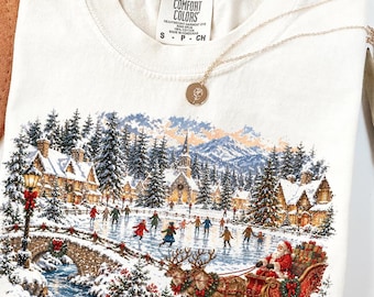 以下が含まれることがあります： クリーム色のTシャツ。凍った池でスケートをする人々、石橋、雪に覆われた家々、そして2頭のトナカイが引くそりに乗ったサンタクロースが描かれた、冬の村の風景のグラフィックがプリントされています。