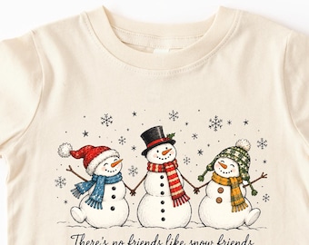 以下が含まれることがあります： クリーム色の半袖Tシャツ。カラフルな冬用帽子とマフラーを身につけた3体の雪だるまのグラフィックが描かれています。雪だるまの下には「There's no friends like snow friends」という文字と、小さな雪の結晶のイラストが添えられています。