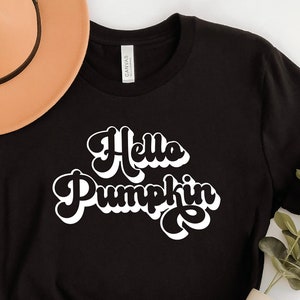 Peut inclure: T-shirt noir avec un texte blanc qui dit "Hello Pumpkin" dans une police rétro.