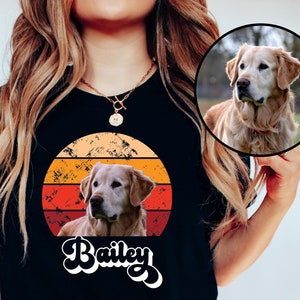 May include: A black t-shirt with a retro sunset graphic featuring a golden retriever dog and the name "Bailey".