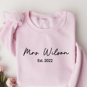 May include: A pink sweatshirt with the text "Mrs. Wilson Est. 2022" in black.