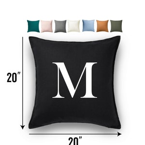 May include: A black square cushion with a white letter "M" in the centre. The cushion is 20 inches by 20 inches.