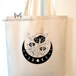 May include: A white canvas tote bag with black handles and a black graphic of mushrooms growing under a crescent moon with stars. The text "MAKEITCUSTOMIZED" is printed on the bag.