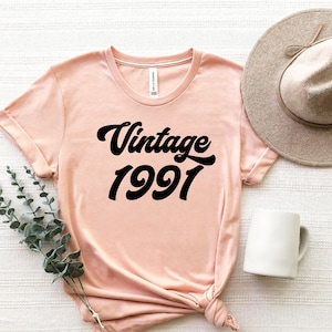 May include: A peach-colored t-shirt with a black vintage 1991 graphic.