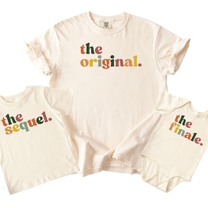 May include: Three cream-coloured t-shirts and a onesie. The largest shirt reads "the original." The smaller shirt says "the sequel." The onesie says "the finale." All text is in a colourful, retro font.