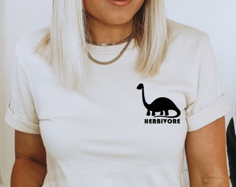 May include: A beige t-shirt with a black dinosaur silhouette and the word "HERBIVORE" printed on the front.