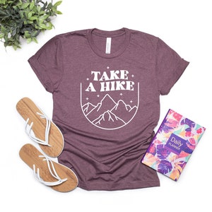 May include: A maroon t-shirt with the text "TAKE A HIKE" in white, featuring a graphic of mountains in a circle.