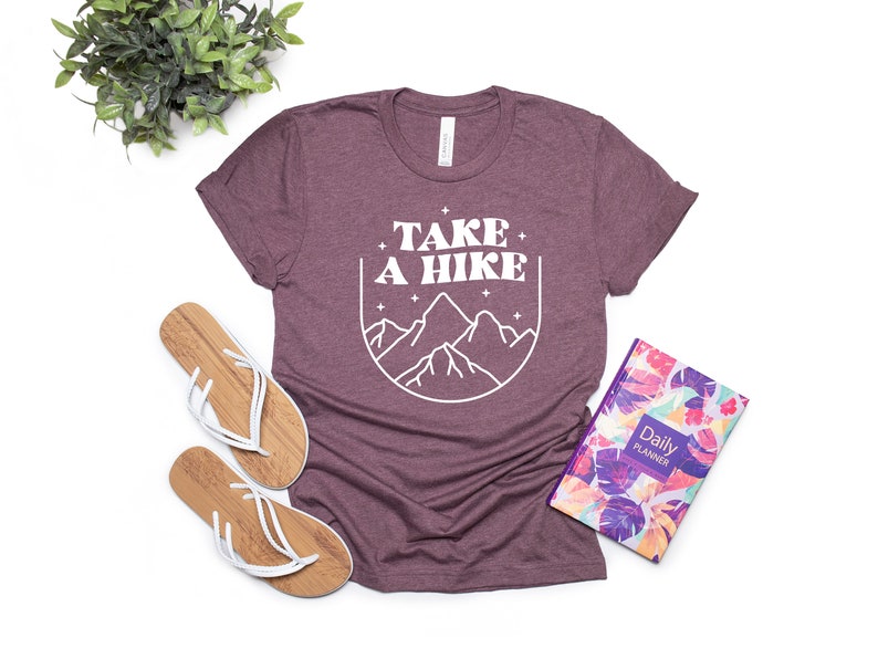 May include: A maroon t-shirt with the text "TAKE A HIKE" in white, featuring a graphic of mountains in a circle.