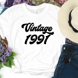 May include: White t-shirt with black text that reads "Vintage 1991" in a retro font.