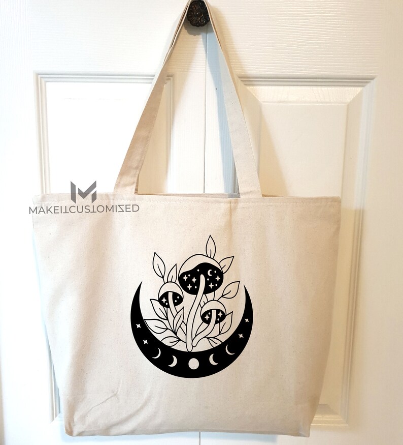 May include: A white canvas tote bag with a black design of mushrooms growing under a crescent moon with stars. The moon has three phases.