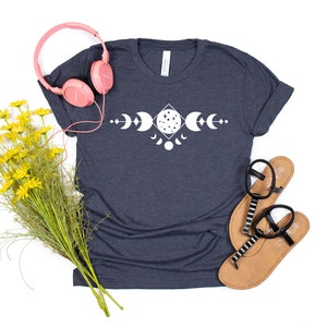 May include: A navy blue t-shirt with a white moon phase design. The design features a crescent moon, a full moon, and a half moon.