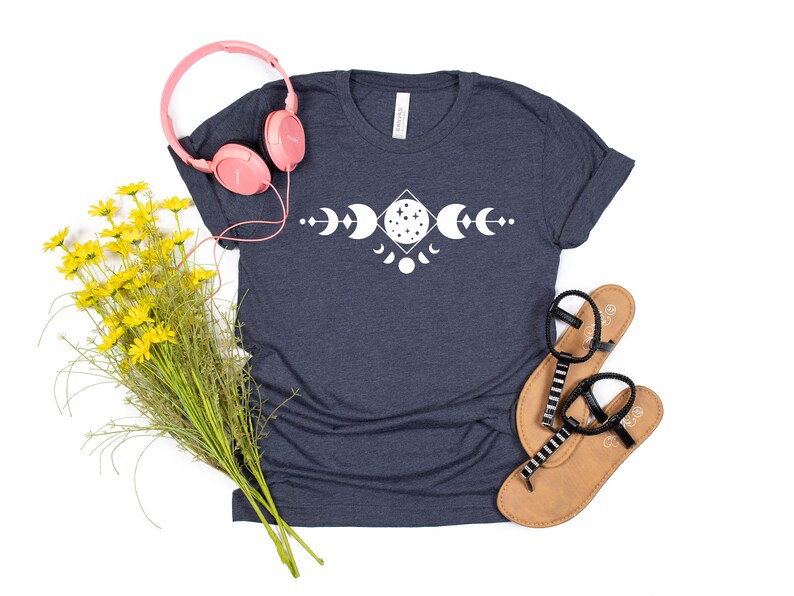 May include: A navy blue t-shirt with a white moon phase design. The design features a crescent moon, a full moon, and a half moon.