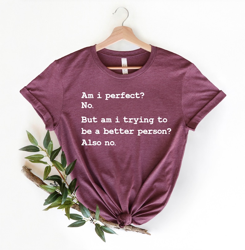 Puede incluir: Camiseta color burdeos con texto blanco que dice "&iquest;Soy perfecto? No. Pero, &iquest;estoy intentando ser una mejor persona? Tampoco."