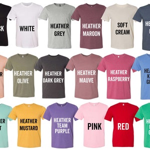 May include: A selection of t-shirts in various colors, including black, white, heather grey, heather maroon, soft cream, heather navy, heather peach, heather olive, heather dark grey, heather mauve, heather raspberry, heather kelly green, heather mint, heather mustard, heather team purple, pink, red, and heather kelly green. The shirts are all short-sleeved and have a crew neck.