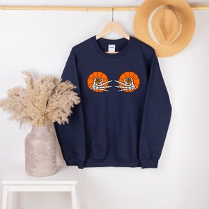 May include: A navy blue sweatshirt with a graphic of two orange pumpkins with skeleton hands reaching out from inside.