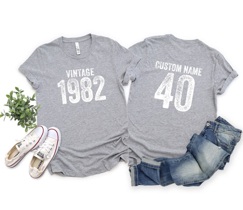 May include: Two gray t-shirts with white text. The front shirt says "Vintage 1982" and the back shirt says "Custom Name 40".