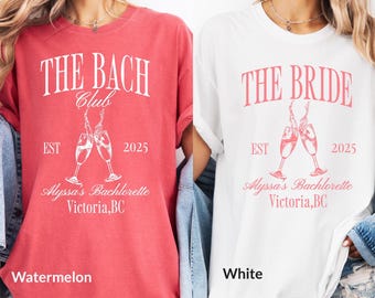 Puede incluir: Dos camisetas, una roja y una blanca, con un tema de despedida de soltera. La camiseta roja dice "The Bach Club" y la camiseta blanca dice "The Bride". Ambas camisetas presentan un gráfico de dos copas de champán brindando, el texto "EST 2025" y el texto "Alyssa's Bachelorette Victoria, BC".
