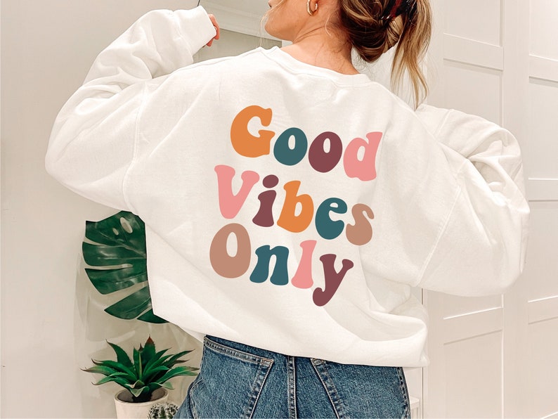 May include: White sweatshirt with the text "Good Vibes Only" in colorful, retro-style lettering.