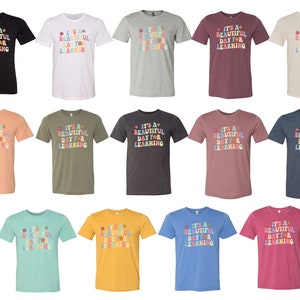 May include: A set of 12 t-shirts in various colors featuring the text "It's a beautiful day for learning" in a colorful retro font with flower accents.