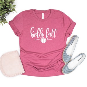 May include: A pink t-shirt with the text "hello fall" in white lettering and a small pumpkin graphic.