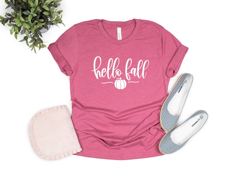 May include: A pink t-shirt with the text "hello fall" in white lettering and a small pumpkin graphic.