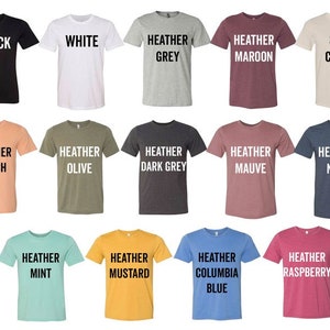 K&ouml;nnte beinhalten: Eine Auswahl an T-Shirts in verschiedenen Farben, darunter Schwarz, Wei&szlig;, Heather Grey, Heather Maroon, Soft Cream, Heather Peach, Heather Olive, Heather Dark Grey, Heather Mauve, Heather Navy, Heather Mint, Heather Mustard, Heather Columbia Blue und Heather Raspberry. Jedes Shirt hat eine andere Farbe und der Farbname ist in wei&szlig;er Schrift aufgedruckt.