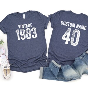 K&ouml;nnte beinhalten: Zwei marineblaue T-Shirts mit wei&szlig;em Text. Das erste Shirt sagt "Vintage 1983" und das zweite Shirt sagt "Custom Name 40".