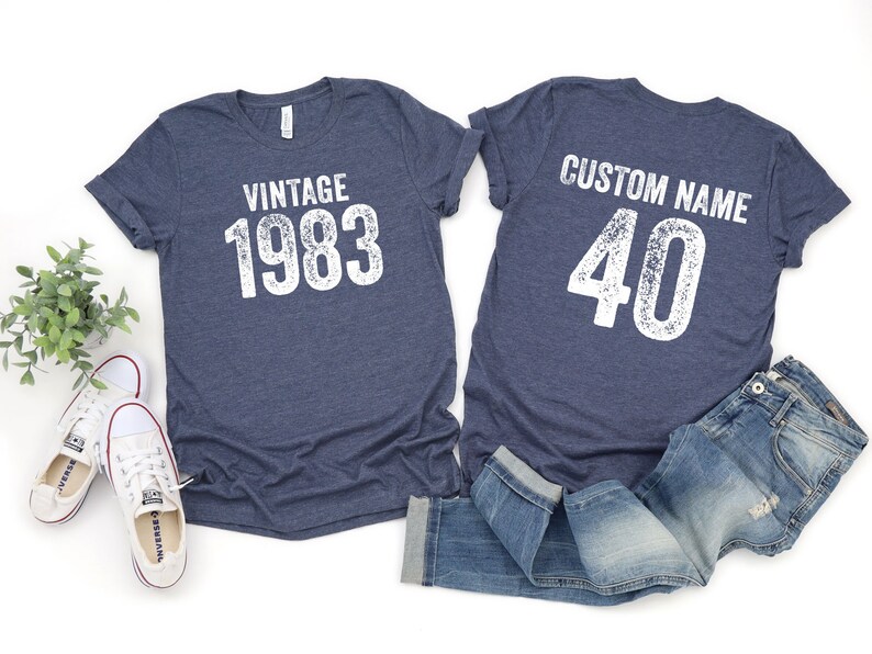 K&ouml;nnte beinhalten: Zwei marineblaue T-Shirts mit wei&szlig;em Text. Das erste Shirt sagt "Vintage 1983" und das zweite Shirt sagt "Custom Name 40".