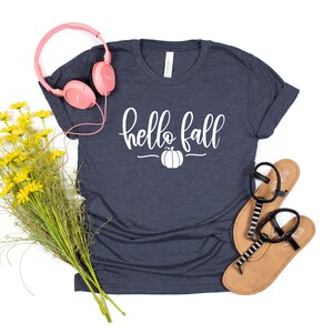 May include: A navy blue t-shirt with the text "hello fall" in white lettering and a white pumpkin graphic.