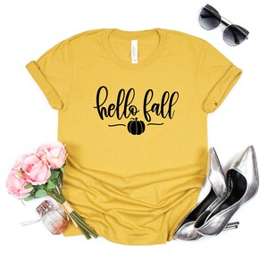 May include: A mustard yellow t-shirt with the text "hello fall" in black script with a small pumpkin graphic underneath.