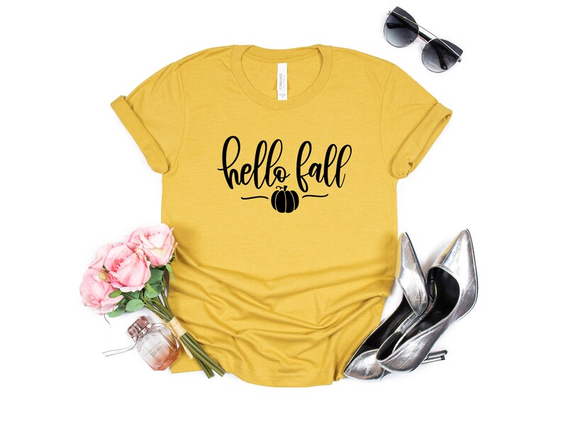 May include: A mustard yellow t-shirt with the text "hello fall" in black script with a small pumpkin graphic underneath.