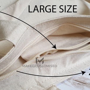 May include: A large, beige canvas tote bag with a zippered pocket. The pocket has a zipper pull and is labeled "ZIPPER". The bag has a large opening and is labeled "LARGE SIZE". The bag also has a smaller pocket on the outside, labeled "POCKET".