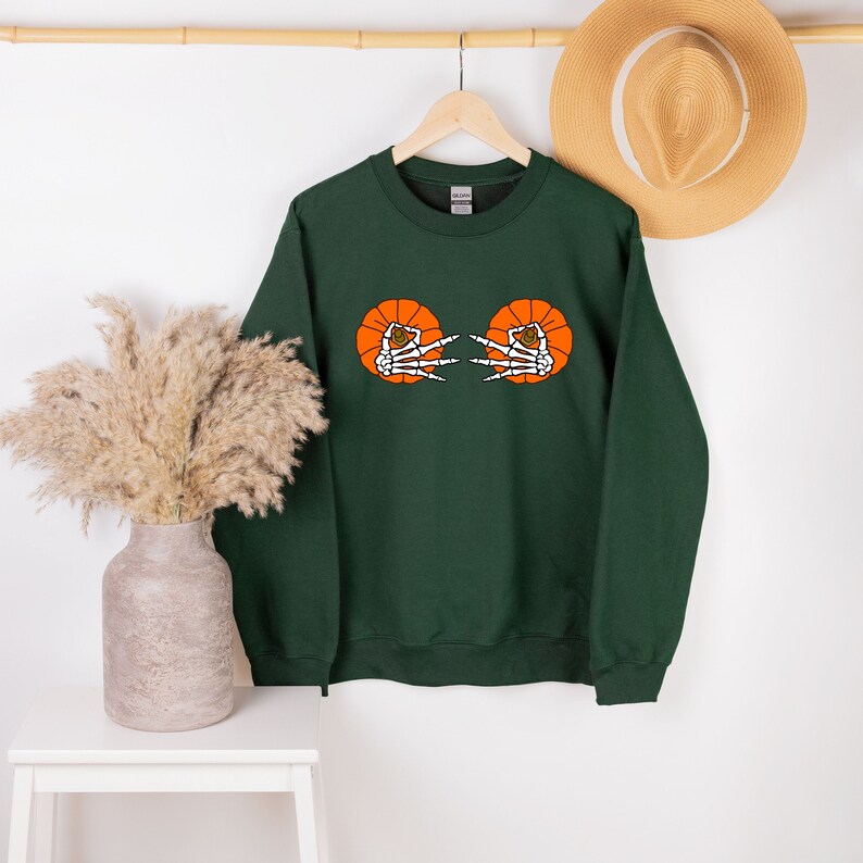 May include: A dark green sweatshirt with a graphic of two orange pumpkins with skeleton hands reaching out from inside.