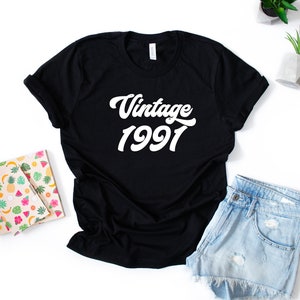 May include: Black t-shirt with white text that reads "Vintage 1991" in a retro font.