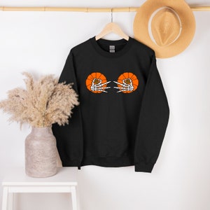 May include: Black sweatshirt with an orange pumpkin design featuring two skeleton hands making the "peace" sign.