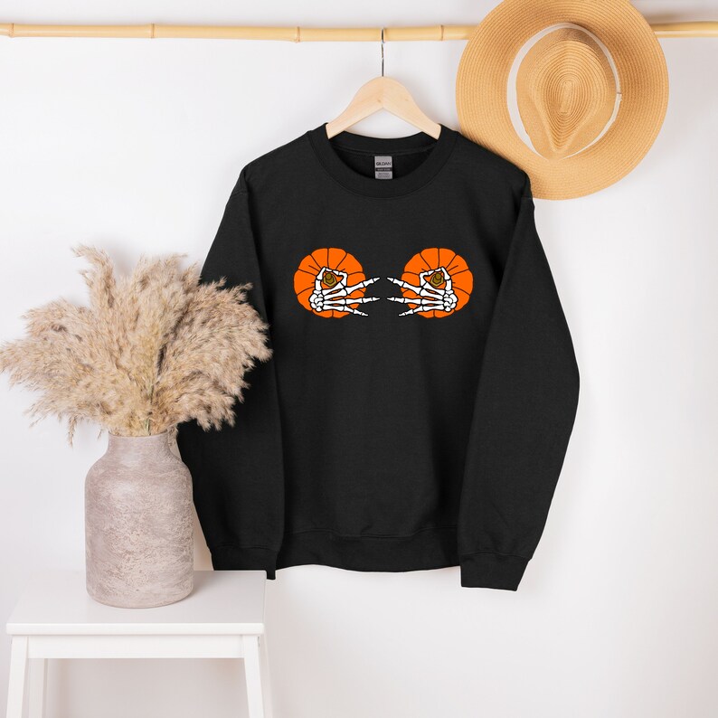 May include: Black sweatshirt with an orange pumpkin design featuring two skeleton hands making the "peace" sign.