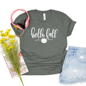 May include: A dark green t-shirt with the text "hello fall" in white lettering and a small white pumpkin graphic.