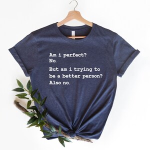 Puede incluir: Una camiseta azul marino con texto blanco que dice: "&iquest;Soy perfecto? No. Pero, &iquest;estoy tratando de ser una mejor persona? Tampoco."