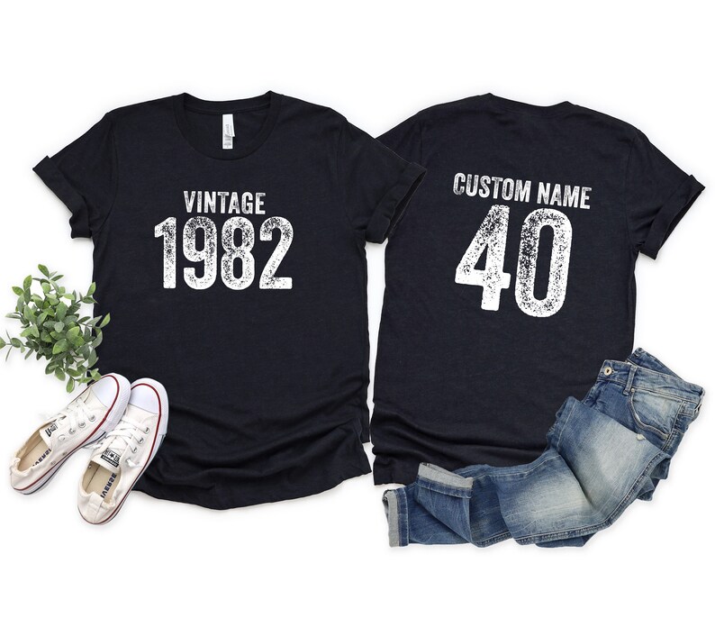 May include: Two black t-shirts with white text. The front shirt says "Vintage 1982". The back shirt says "Custom Name 40".