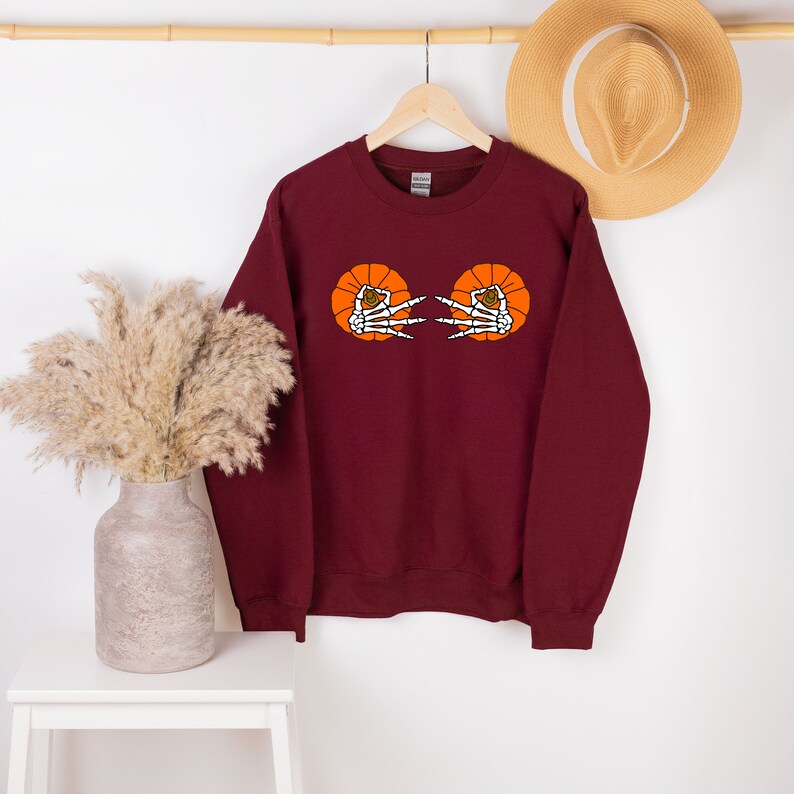 May include: Burgundy sweatshirt with a graphic of two orange pumpkins with skeleton hands reaching out from the inside.