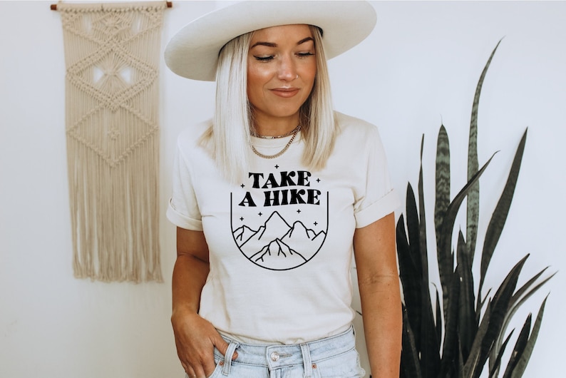 May include: A white t-shirt with a black graphic design that says "TAKE A HIKE" with a mountain range and stars inside a circle.